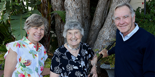 Two female and one eldery male standing next to a tree